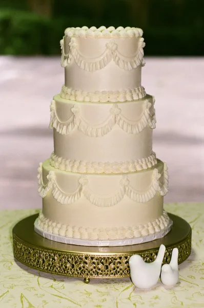 Wedding cake, a four tier wedding cake with ivory buttercream on a gold cake stand, set against garden greenery and a pale backdrop