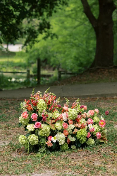 Ground floral arrangement, a lush ground floral installation with roses, layered on a grass lawn near trees and a wooden fence.
