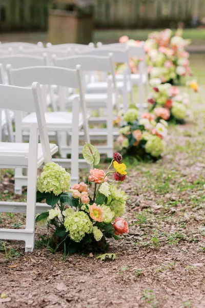 Ceremony aisle flowers arranged as aisle meadow florals bloom with hydrangeas along a grass lawn, framed by a dirt path and a wooden garden fence.