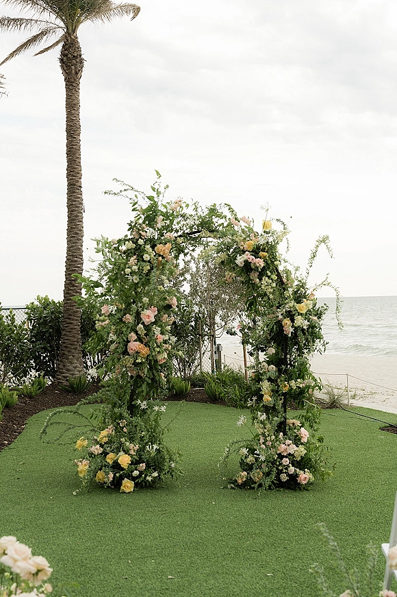 Wedding ceremony arch with a floral wedding arch of roses and cascading greenery on a lawn overlooking the ocean and palm trees