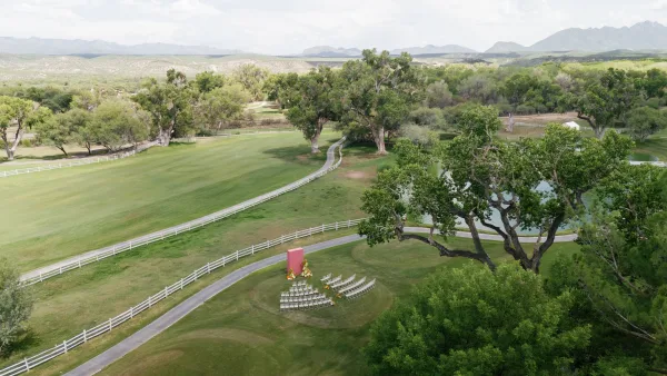 Outdoor ceremony setup with modern ceremony decor, rows of ceremony chairs on a grassy lawn overlooking a pond with mountain views under open sky.