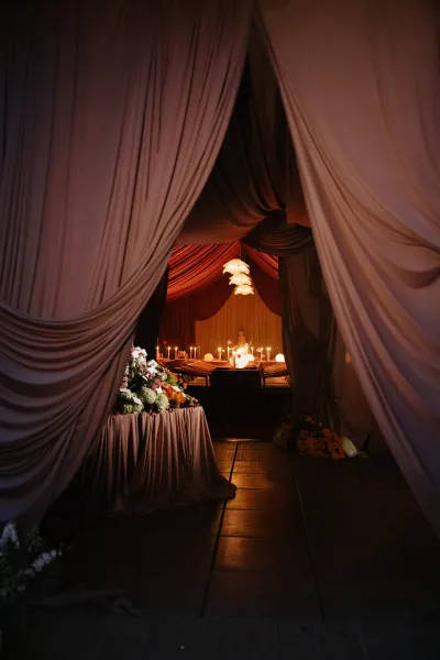 Reception tablescape for a candlelit wedding dinner beneath pendant lights, framed by a draped entry and styled for an intimate evening.
