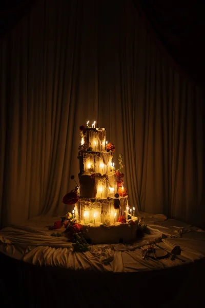 Wedding cake in a candlelit cake display, a tiered buttercream with red florals and grapes, finished with a gold cutting set.