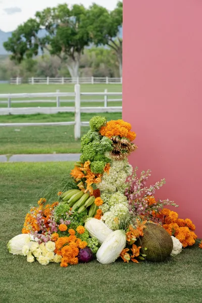 Ceremony floral installation, a lush ground floral arrangement with marigolds, set on a grass lawn with distant mountains under open sky.