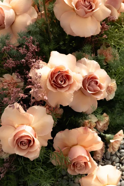 Wedding floral arrangement with peach rose arrangement, greenery and filler blooms set low on gravel stones for ceremony decor