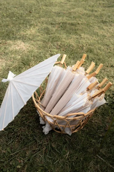 Wedding parasols with paper parasols wedding display in a wicker basket, white canopies with wooden handles resting on a grass lawn