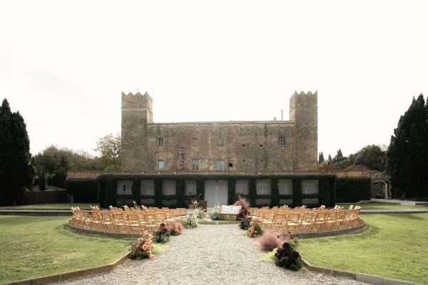 Ceremony setup with wood folding chairs in a semi circle, lined by aisle florals on a gravel aisle before a stone castle facade