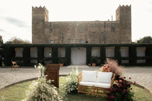Wedding ceremony setup with outdoor ceremony altar, featuring a wood podium and wicker loveseat with florals before an ivy castle wall