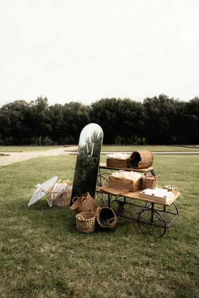 Welcome table decor with a mirror welcome sign on a vintage cart, wooden crates and paper parasols on a lawn by trees and path