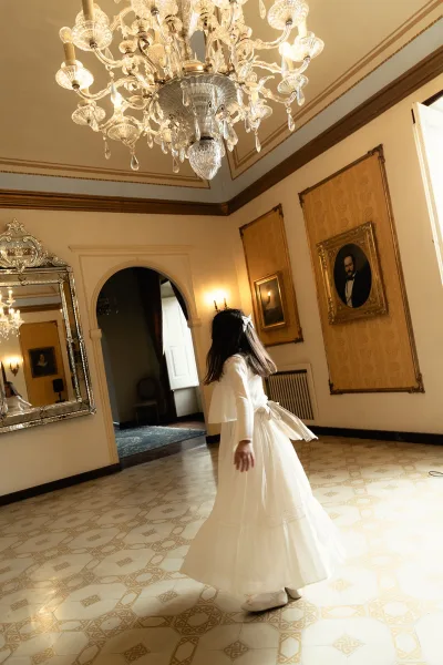 Bridal portrait of a bride twirling her tulle skirt in a long sleeve wedding dress beneath a chandelier in an ornate cream-and-gold room