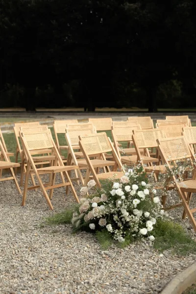 Ceremony seating with outdoor wedding ceremony chairs, wood folding and cane chairs lined on gravel with aisle floral clusters and greenery