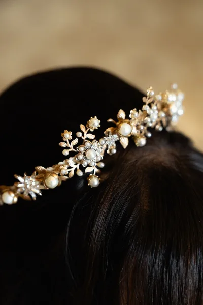 Bridal hair accessory with a pearl wedding headpiece, gold hair vine and crystal rhinestones pinned into dark hair against a blurred backdrop