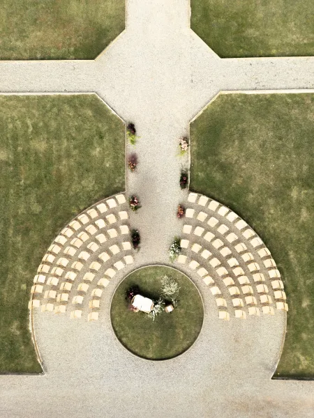 Ceremony seating layout in a semi-circle of chairs with greenery and white florals lining a gravel aisle on a courtyard lawn path