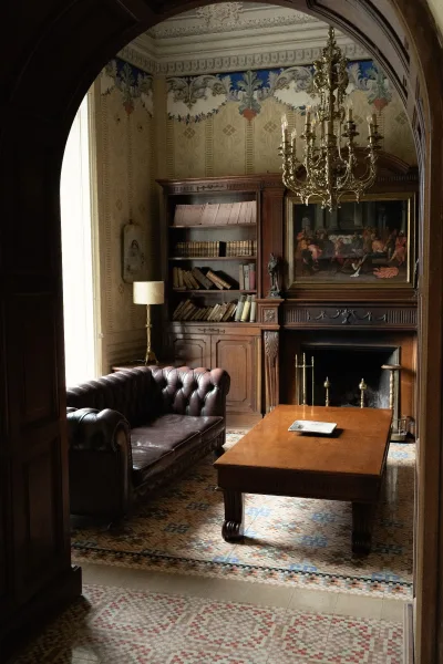 Vintage lounge area wedding cocktail lounge with a leather chesterfield sofa, brass chandelier, and fireplace by built-in bookcases in a historic interior