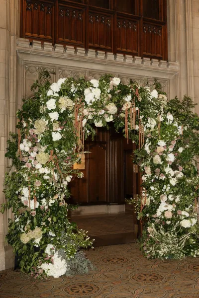 Wedding floral arch forms a romantic doorway flower arch with hydrangeas, framed by a stone archway and tall wooden doors.