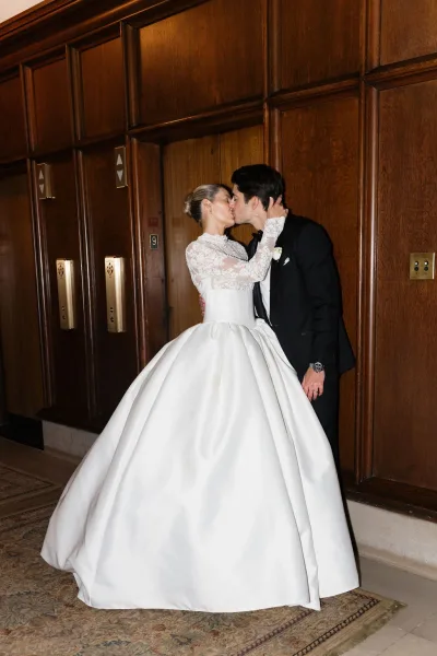 Wedding kiss portrait of the bride and groom, an indoor wedding portrait framed by elevator doors and wood paneling, with lace sleeves.