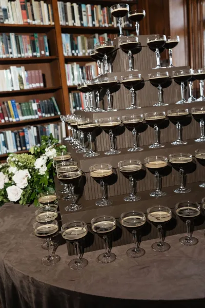Espresso martini tower as a signature cocktail display, accented with white roses, framed by bookshelves filled with books and warm wood paneling.