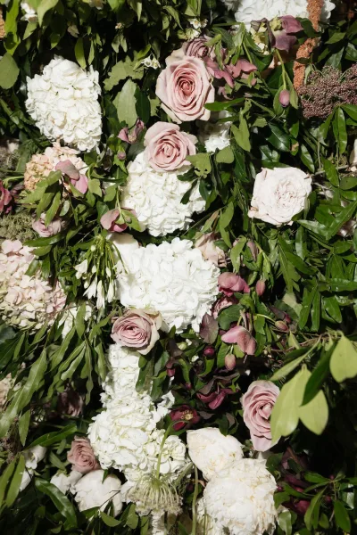 Floral installation creating a lush flower wall backdrop, densely layered with roses against a tapestry of green leaves.
