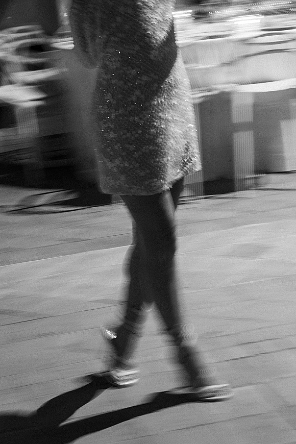 Wedding guest dancing in a sequined dress and high heels on the dance floor, with stage equipment and blurred reception lights behind