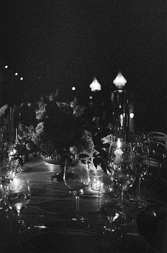 Reception tablescape with a candlelit wedding table featuring lanterns, wine glasses, and floral greenery garland beneath string lights at night