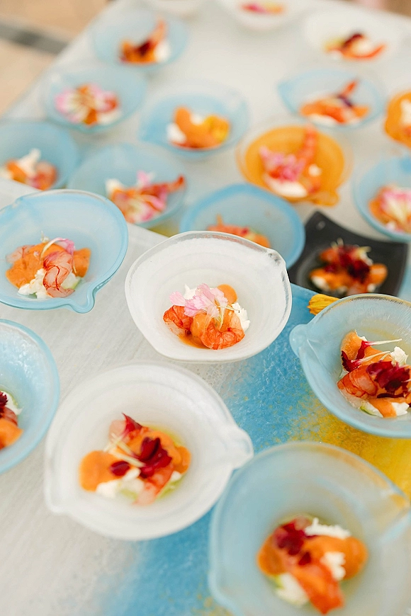 Wedding appetizer tasting bowls with shrimp, sauce, microgreens, and edible flower garnish on a white tablecloth serving table