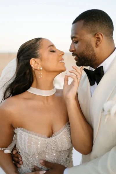 Wedding couple portrait of bride and groom close up, forehead touching under a bright sky, bride in veil and beaded dress with pearl earrings