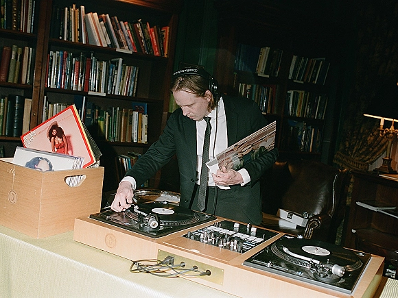 Wedding DJ at a wedding DJ setup mixing vinyl on turntables and mixer, wearing headphones and suit in a library with bookshelves