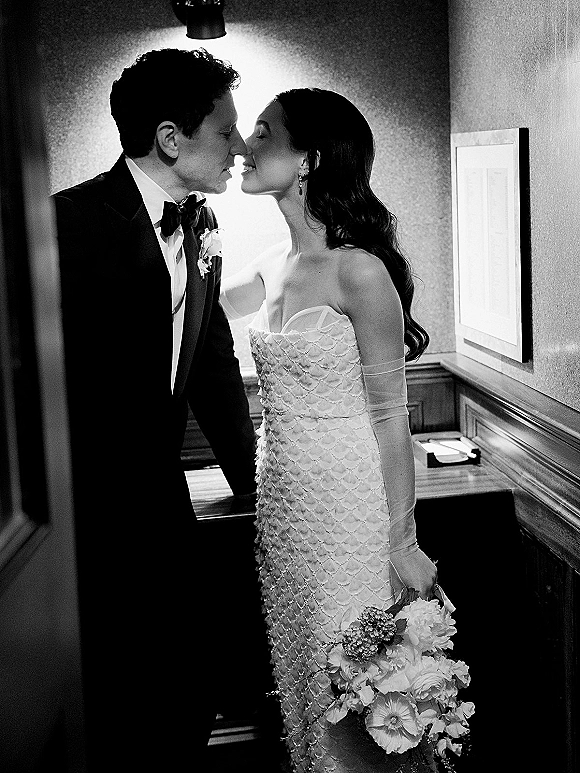 Wedding kiss portrait of bride and groom kiss in a hallway, her strapless textured dress and long gloves beside his tuxedo boutonniere