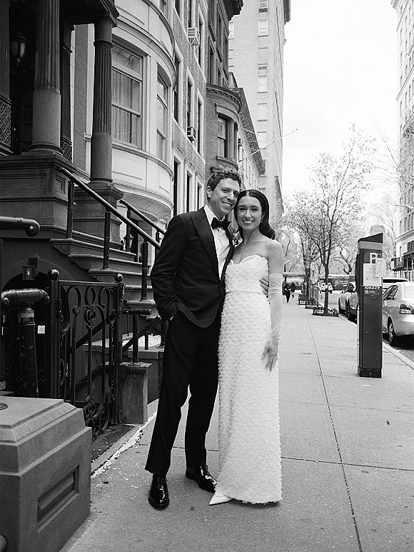 Couple portrait in black and white, bride in strapless dress and opera gloves with groom in tuxedo on a brownstone sidewalk stoop