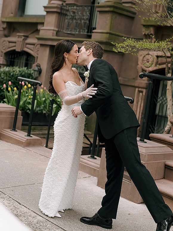 Wedding kiss portrait of bride and groom kissing on brownstone steps, bride in strapless dress with tulle gloves, groom in black tuxedo