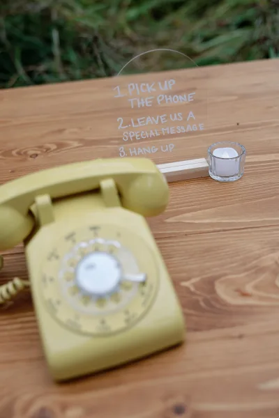 Wedding guestbook phone audio guestbook phone with a yellow vintage rotary handset beside an acrylic instruction sign on a wooden table outdoors