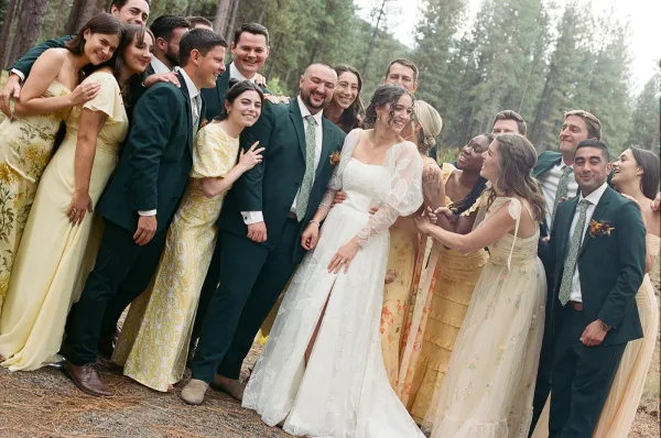 Wedding party portrait of bride with wedding party laughing on a forest dirt path, bridesmaids in yellow dresses and groomsmen in dark suits