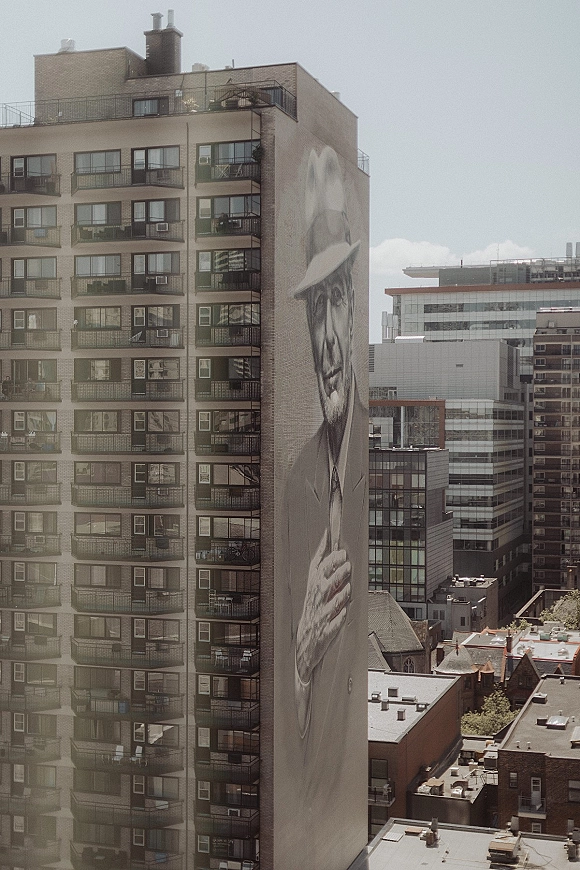 City building mural with a large scale wall mural portrait across an apartment facade, balconies and windows above downtown rooftops and skyline