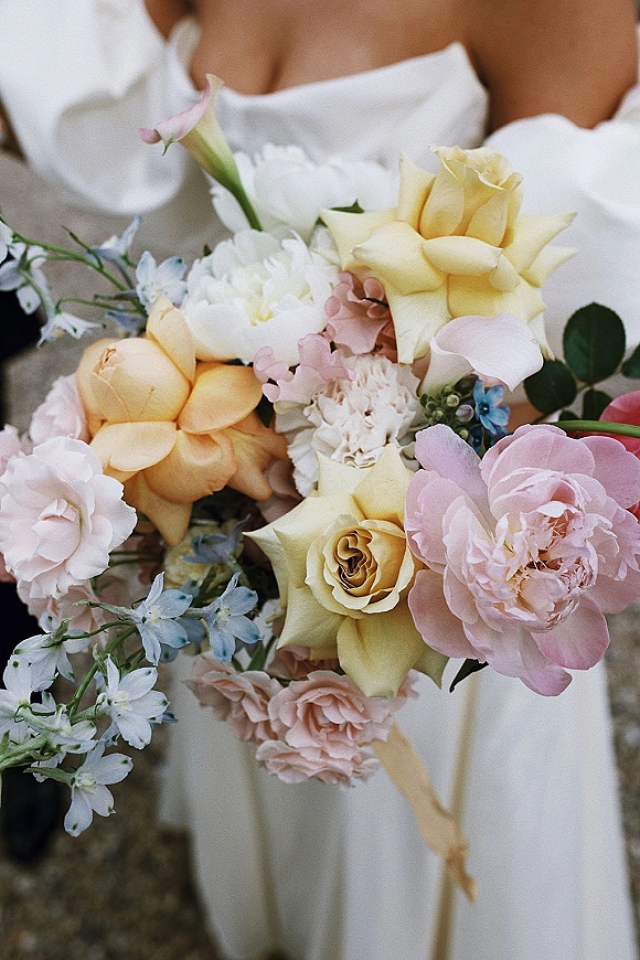 Bridal bouquet with pastel wedding bouquet blooms of garden roses, peony, calla lily and delphinium, tied with ribbon against outdoor ground