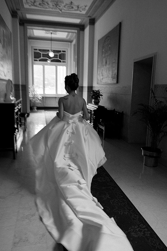 Bridal portrait of a bride walking away in a strapless ball gown with a long train, lit by tall hallway windows and classic moldings