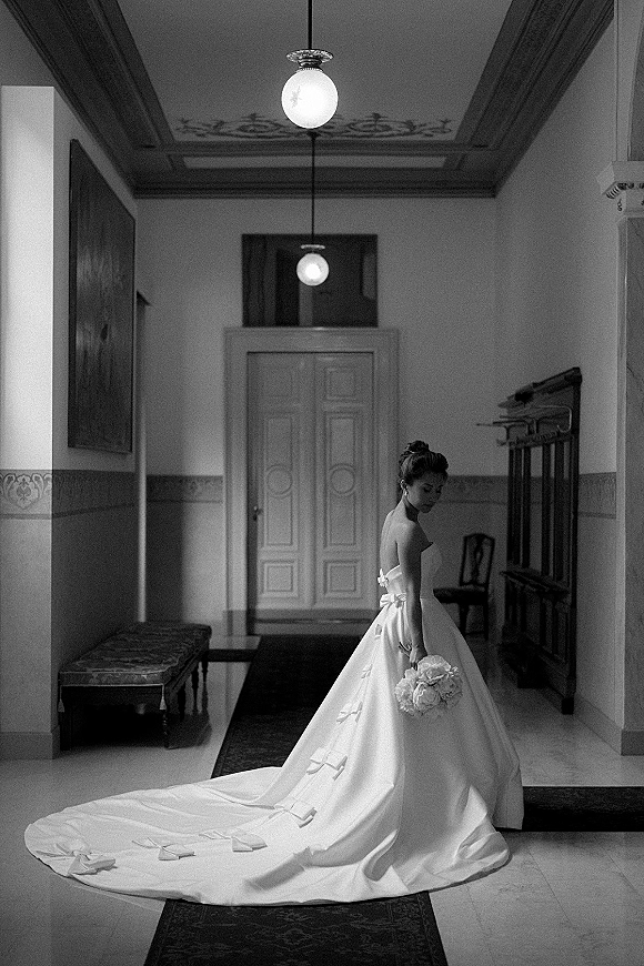 Bridal portrait in a black and white bridal portrait style, bride in strapless gown with long train holding bouquet in an indoor hallway