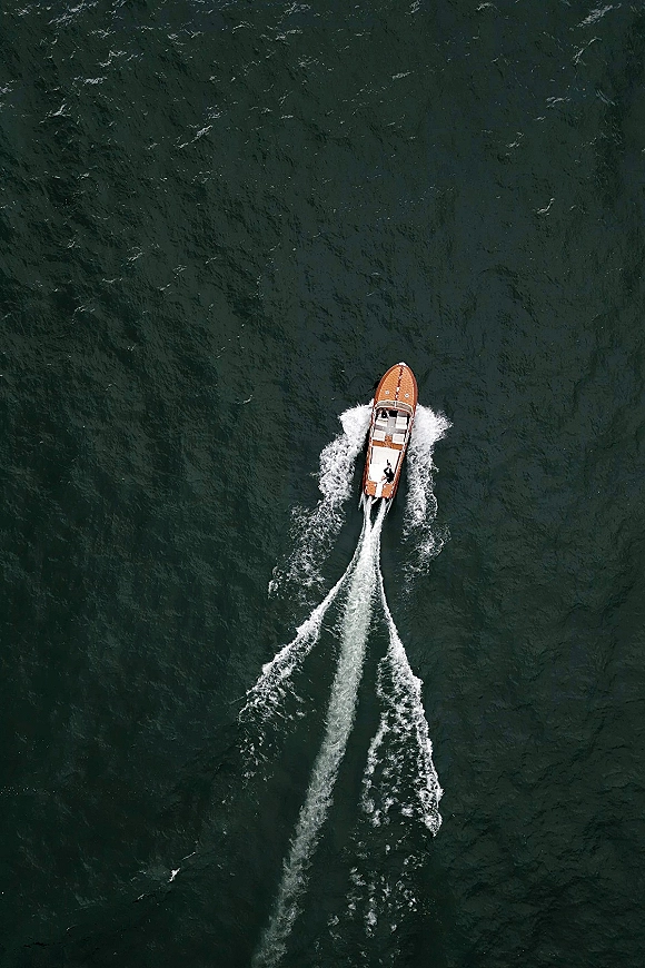 Wedding getaway boat speeding across open water, wooden motorboat leaving a bright wake as newlyweds make their wedding boat exit