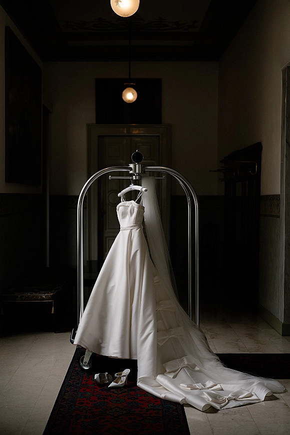 Wedding dress on a hanger, strapless wedding dress with a long veil draped over a garment rack in a hallway with pendant lights