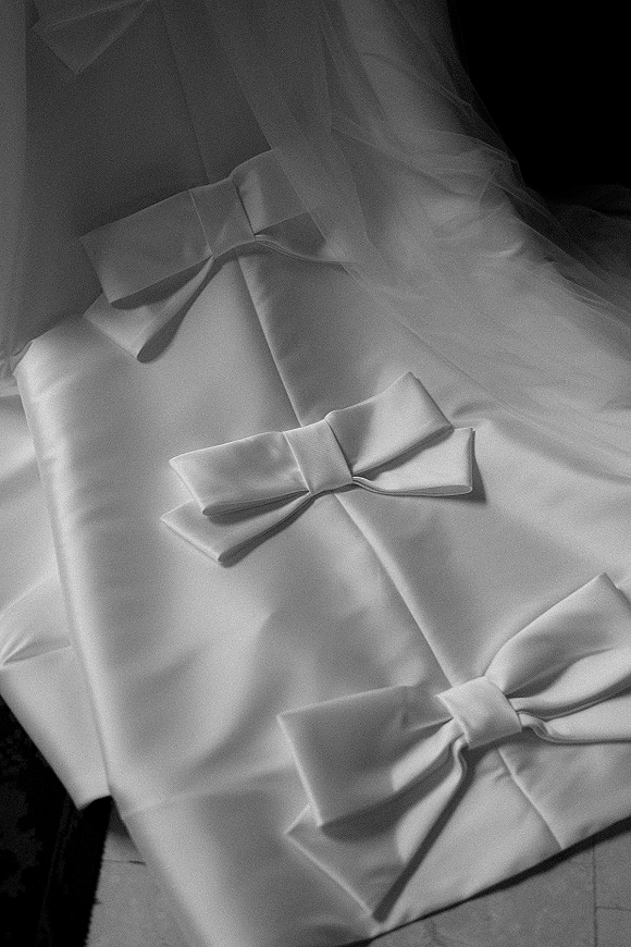Wedding ring box in satin with a bow detail, resting on soft tulle fabric on a dark surface for an elegant bridal flat lay detail