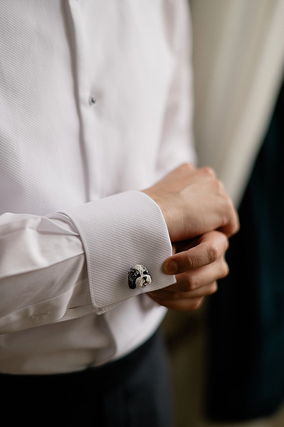 Groom cufflinks with novelty cufflinks featuring a dog design on French-cuff white dress shirt sleeves, neutral indoor setting