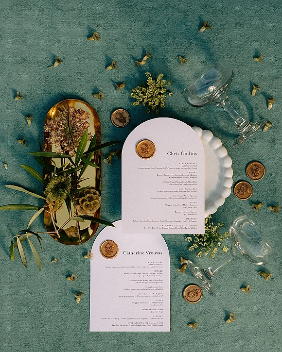 Wedding menu cards with wax seals on a gold tray and scalloped plate, styled with dried florals on a teal linen tablescape with petals