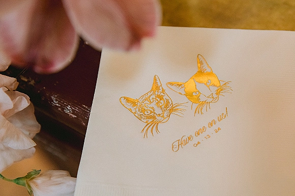 Wedding guest book with wedding guestbook message beside a gold foil cat illustration, open on a wood table with white flowers