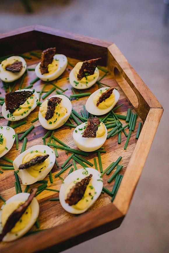 Wedding appetizers of deviled egg appetizer halves topped with chives arranged neatly on a wooden serving tray on a tabletop