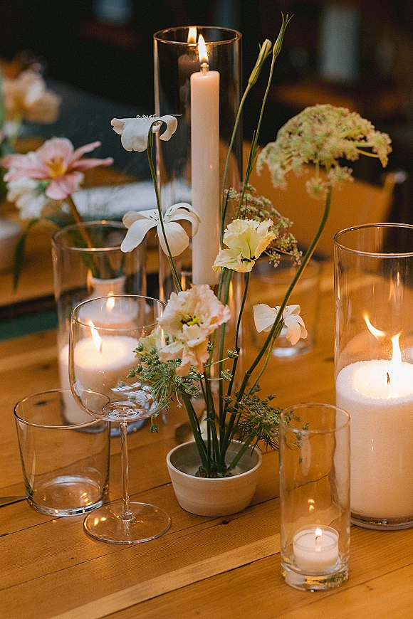 Wedding centerpiece with candlelit wedding centerpiece glow, taper candle and wildflowers in bud vases on a wood table at an indoor reception space