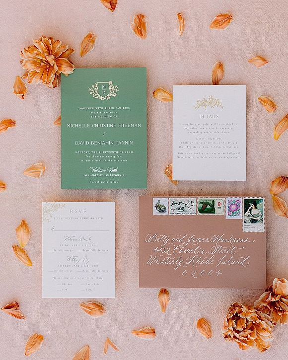 Invitation suite wedding invitation flat lay with sage green cards, calligraphy envelope, vintage stamps, and petals on linen backdrop