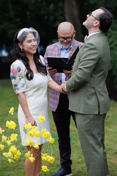 Ceremony moment of the couple exchanging wedding vows as the bride in a short wedding dress clasps hands with the groom.