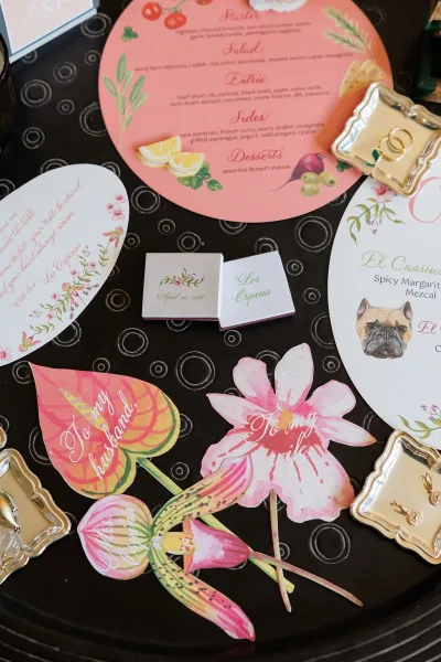 Wedding stationery flat lay featuring a menu card design with a gold ring dish on a black tray over a dark tabletop