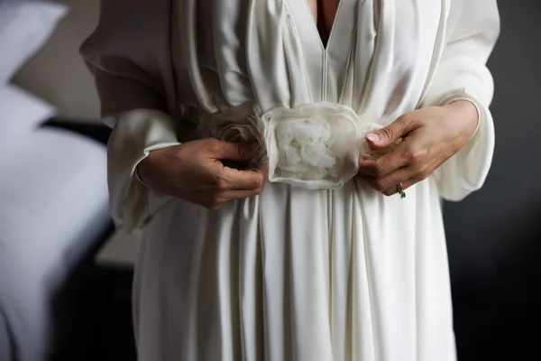 Wedding dress belt with a fabric flower accent cinching an ivory bridal gown, a refined bridal waist embellishment captured in close view.