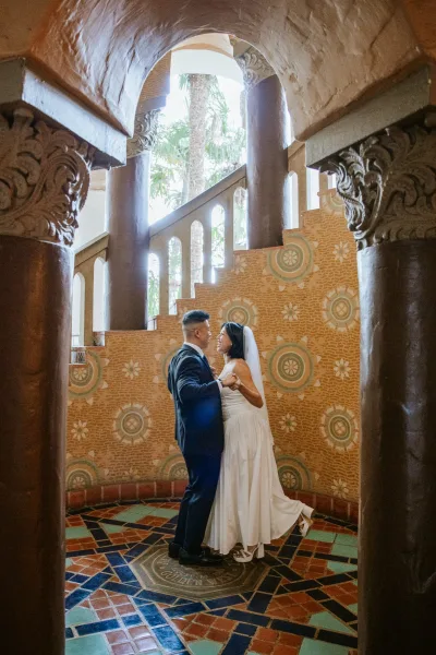 Couple portrait of bride in a strapless tea-length dress and veil dancing with groom in black suit by an arched tiled doorway