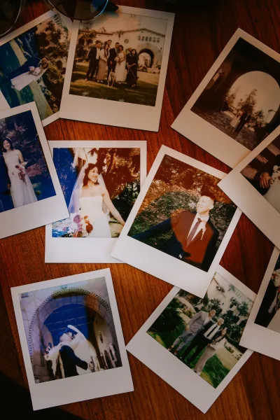 Wedding polaroids and instant film wedding photos scattered on a wood table, showing bride and groom portraits, bouquet, veil, and suit details
